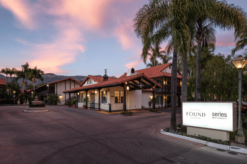 Exterior view of Found Hotel with courtyard, palm trees, and lit buildings at dusk