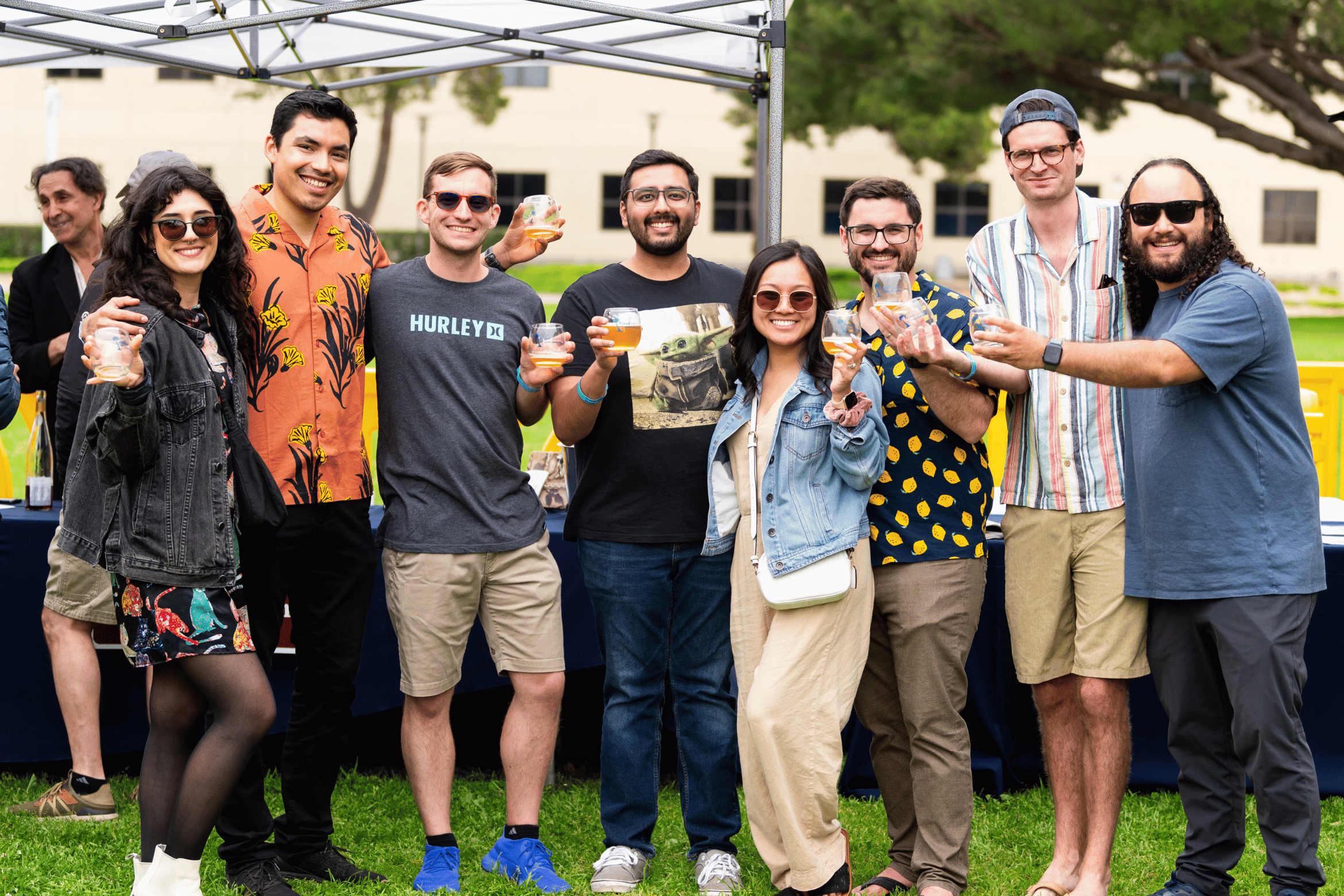 A cheerful group of alums raises their glasses for a toast during a sunny outdoor gathering.